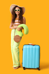 Sticker - Happy young African-American woman in sunglasses with suitcase and travel pillow on yellow background