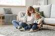 © Pixel-Shot - Happy mother and her little son reading book on floor in living room at home