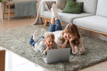 Wall Mural - Happy mother and her little son with laptop lying on floor in living room at home