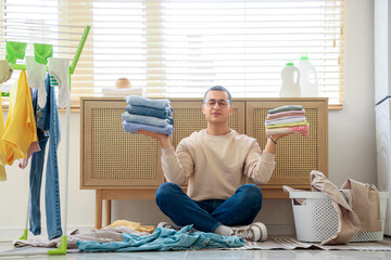 Sticker - Young man meditating with stacks of clean clothes in laundry room