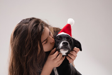 teenage girl kissing her dog wearing a santa hat for christmas c