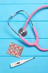 Canvas Print - Stethoscope, thermometer and pills on light blue wooden background, flat lay. Medical treatment