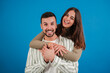 © Jose Calsina - Young adult couple laughing and looking at camera against blue studio backdrop. Caucasian girlfriend giving a hug to her boyfriend and smiling together. Happy woman embracing her handsome partner