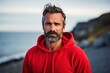 © MediaRaw - A man with a beard and a red hoodie is standing on a beach