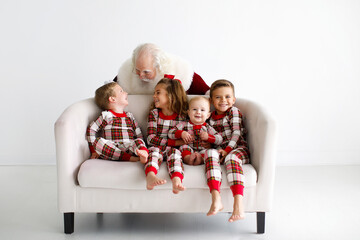 Santa with four kids in plaid pajamas on a white sofa, smiling a