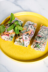 Canvas Print - Close-up of fresh spring rolls on a yellow plate with a mint garnish