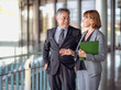 © Nassorn - Portrait of mature Asian businessman and well-dressed Caucasian businesswoman standing in office working together. Two diverse colleagues, group of confident professional business people. Diversity.