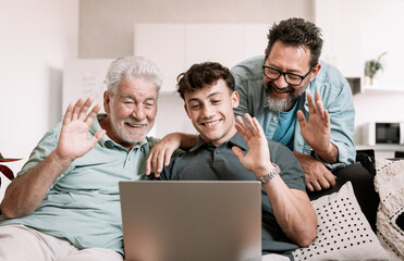 Sticker - Video call concept. Happy multigenerational family sitting on sofa using laptop technology for webcam connection - grandfather with mature son and young grandson enjoying carefree moments together