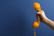 © New Africa - Woman holding orange telephone handset on blue background, closeup. Space for text