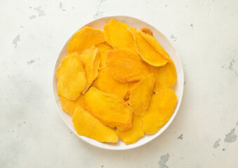 Wall Mural - Round plate with dried mango pieces on light background.