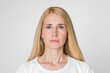 © Prostock-studio - This image shows a woman with blonde hair looking directly at the camera with a neutral expression. She is wearing a white t-shirt and has a light complexion. The background is a plain white wall.