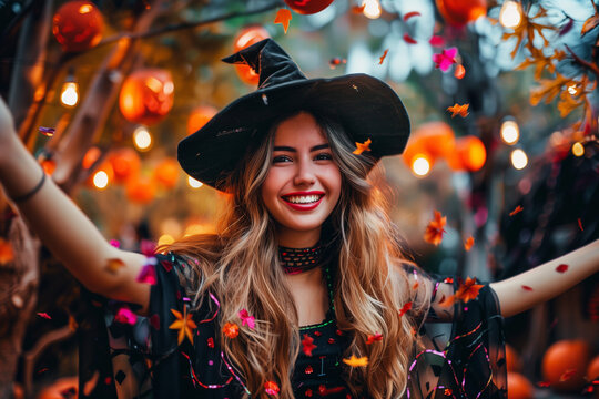 Halloween party. Portrait of a happy smiling young woman. Girl in a witch costume, black hat and dress. Evening, pumpkin lights and garlands, confetti. Celebration, halloween festival.