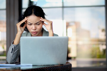 Tensed businesswoman puts head in hands in front laptop at office workplace. Woman suffers from a headache, rubs temples with fingers closing eyes in pain. Tired female officer feels stress with a job