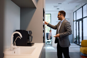 happy businessman preparing himself cup of coffee in office kitchen.