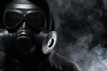 Man wearing gas mask in smoke on black background, closeup. Space for text