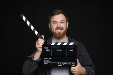 Poster - Making movie. Smiling man with clapperboard on black background