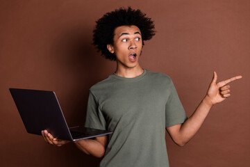 Sticker - Photo portrait of young guy in gray t shirt remote holding netbook point finger mockup surprised isolated on brown color background