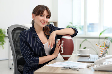 Canvas Print - Smiling employee with american football ball at table in office