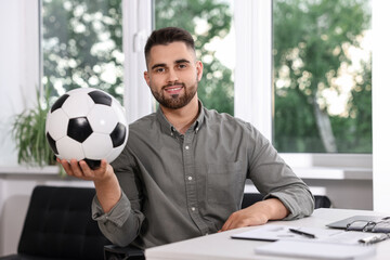 Wall Mural - Young man with soccer ball at table in office