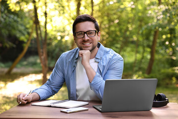 Canvas Print - Smiling freelancer with laptop at table outdoors. Remote job