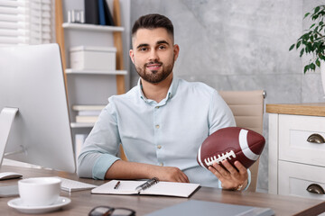 Wall Mural - Young man with american football ball at table in office