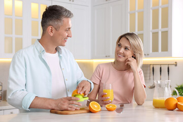 Poster - Happy couple with juicer and fresh products making juice at white marble table in kitchen