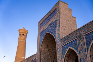 Wall Mural - A tall building with a blue archway and a tower in the background. The sky is clear and blue