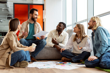 Group of young people having business meeting sitting on floor in modern office