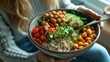 © Intelligent Horizons - Close up view of a woman enjoying a nutritious and colorful Buddha bowl filled with quinoa chickpeas roasted vegetables and fresh greens  The vibrant dish represents a balanced healthy