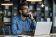 © btiger - Focused young businessman in blue shirt working on laptop at desk in office thinking about project