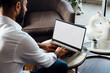 © AlexPhotoStock - Over shoulder view of a young business man using computer laptop in front of an blank white computer screen in his home living room. Photo ready for mockup.