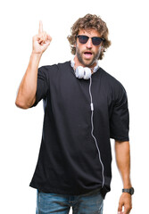 Wall Mural - Handsome hispanic man listening to music wearing headphones over isolated background pointing finger up with successful idea. Exited and happy. Number one.