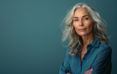 Wall Mural - A woman with gray hair is wearing a blue shirt and is looking at the camera. She has her arms crossed and she is confident and self-assured