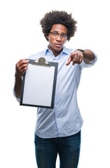 Sticker - Afro american man holding clipboard over isolated background pointing with finger to the camera and to you, hand sign, positive and confident gesture from the front