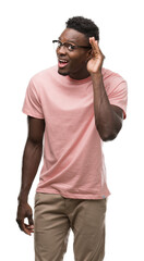 Sticker - Young african american man wearing pink t-shirt smiling with hand over ear listening an hearing to rumor or gossip. Deafness concept.