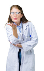 Canvas Print - Middle age mature doctor woman wearing medical coat over isolated background looking at the camera blowing a kiss with hand on air being lovely and sexy. Love expression.