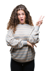 Wall Mural - Beautiful brunette curly hair young girl wearing winter sweater over isolated background smiling with happy face winking at the camera doing victory sign. Number two.