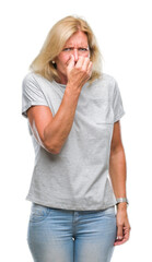 Sticker - Middle age blonde woman over isolated background smelling something stinky and disgusting, intolerable smell, holding breath with fingers on nose. Bad smells concept.