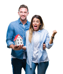 Wall Mural - Young couple in love holding house over isolated background screaming proud and celebrating victory and success very excited, cheering emotion