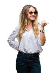 Sticker - Young beautiful blonde woman wearing sunglasses over isolated background smiling with happy face looking and pointing to the side with thumb up.