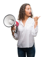 Wall Mural - Young hispanic woman holding megaphone pointing and showing with thumb up to the side with happy face smiling