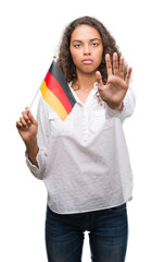 Canvas Print - Young hispanic woman holding flag of Germany with open hand doing stop sign with serious and confident expression, defense gesture