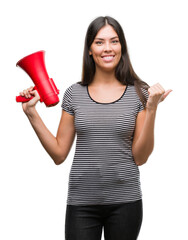 Wall Mural - Young hispanic woman holding megaphone pointing and showing with thumb up to the side with happy face smiling