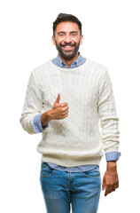 Wall Mural - Adult hispanic man wearing winter sweater over isolated background doing happy thumbs up gesture with hand. Approving expression looking at the camera with showing success.