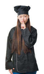 Sticker - Young Chinese woman over isolated background wearing chef uniform asking to be quiet with finger on lips. Silence and secret concept.