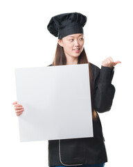 Poster - Young Chinese woman over isolated background wearing chef uniform holding banner pointing and showing with thumb up to the side with happy face smiling