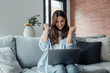 © Daniel - Excited emotional screams with joy woman sit on sofa hold on lap notebook makes Yes hand gesture feels happy getting job of dream, e-mail sales discount special offer, on-line lottery victory concept.