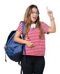 Sticker - Young beautiful brunette student woman wearing headphones and backpack over isolated background pointing finger up with successful idea. Exited and happy. Number one.