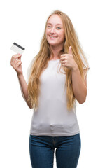 Sticker - Blonde teenager woman holding credit card happy with big smile doing ok sign, thumb up with fingers, excellent sign