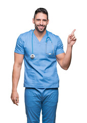 Wall Mural - Handsome young doctor surgeon man over isolated background with a big smile on face, pointing with hand and finger to the side looking at the camera.